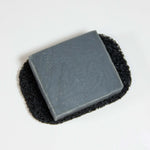 Photo of a black soap saver pad with a bar of soap sitting on top. Isolated on a white background.