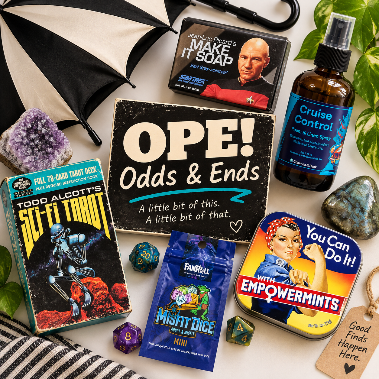 Eclectic Ope! Odds & Ends collection featuring novelty soap, room spray, sci-fi tarot cards, gaming dice, Empowermints, crystals, and a black-and-white umbrella.
