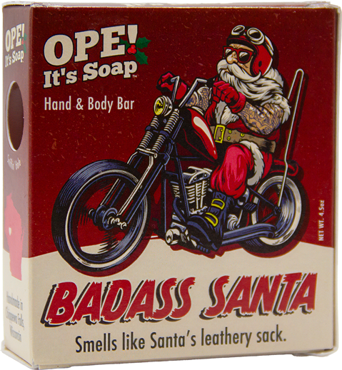 Ope! It’s Soap Badass Santa soap box featuring a tattooed Santa in biker gear riding a motorcycle, with bold red and cream packaging and the tagline “Smells like Santa’s leathery sack.”