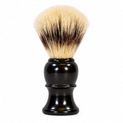 A shaving brush with a glossy black plastic handle and dense bristles that are cream and dark brown, photographed on a solid white background.