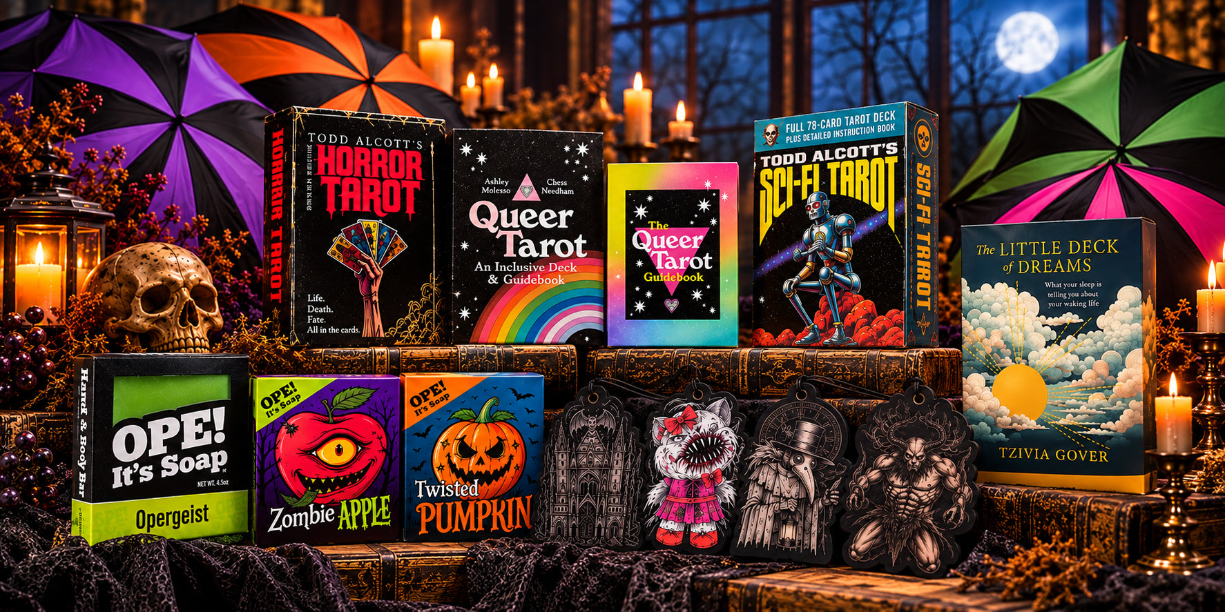 Halloween collection featuring Ope! It's Soap seasonal soaps, gothic air fresheners, tarot decks, dream cards, and colorful batwing umbrellas displayed among antique books, candles, and a skull in a spooky, moonlit setting.