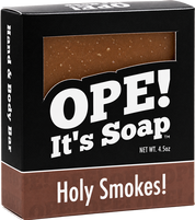 Ope! It’s Soap Holy Smokes soap box featuring black and warm brown packaging with a window showing the speckled brown soap bar inside.