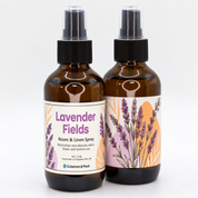 Two amber glass Lavender Fields room and linen spray bottles featuring purple lavender botanical labels, black spray tops, and clear caps.