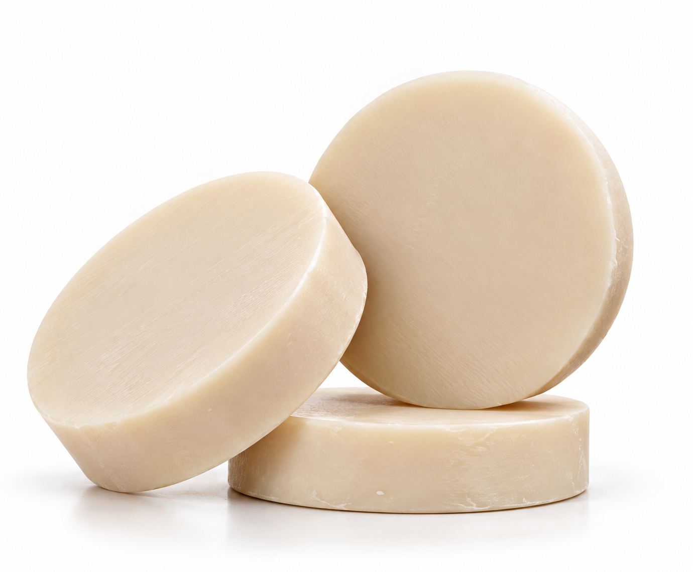 Three cream colored round shampoo bars arranged on a white background, with one lying flat, one tilted at an angle, and one standing upright.