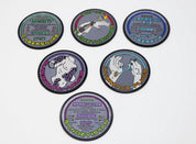Six Cyberpunk RED collectible metal cybergear coins arranged on white, featuring Cybersnake, Pop-Up Flamethrower, Artificial Eye, Subdermal Armor, Interface Plugs, and Sandevistan designs.