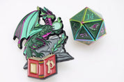 Close-up of Pathfinder Lost Tome Mirage Dragon collectible pinature featuring a green and purple dragon holding a glowing orb above an open red book, displayed beside a matching iridescent green metal D20 die.