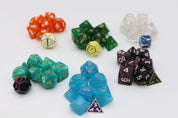 Assorted polyhedral RPG dice sets in orange, green, clear, turquoise, blue, and black with purple accents. Each colorful plastic dice set is paired with a contrasting metal die, displayed on a white background.