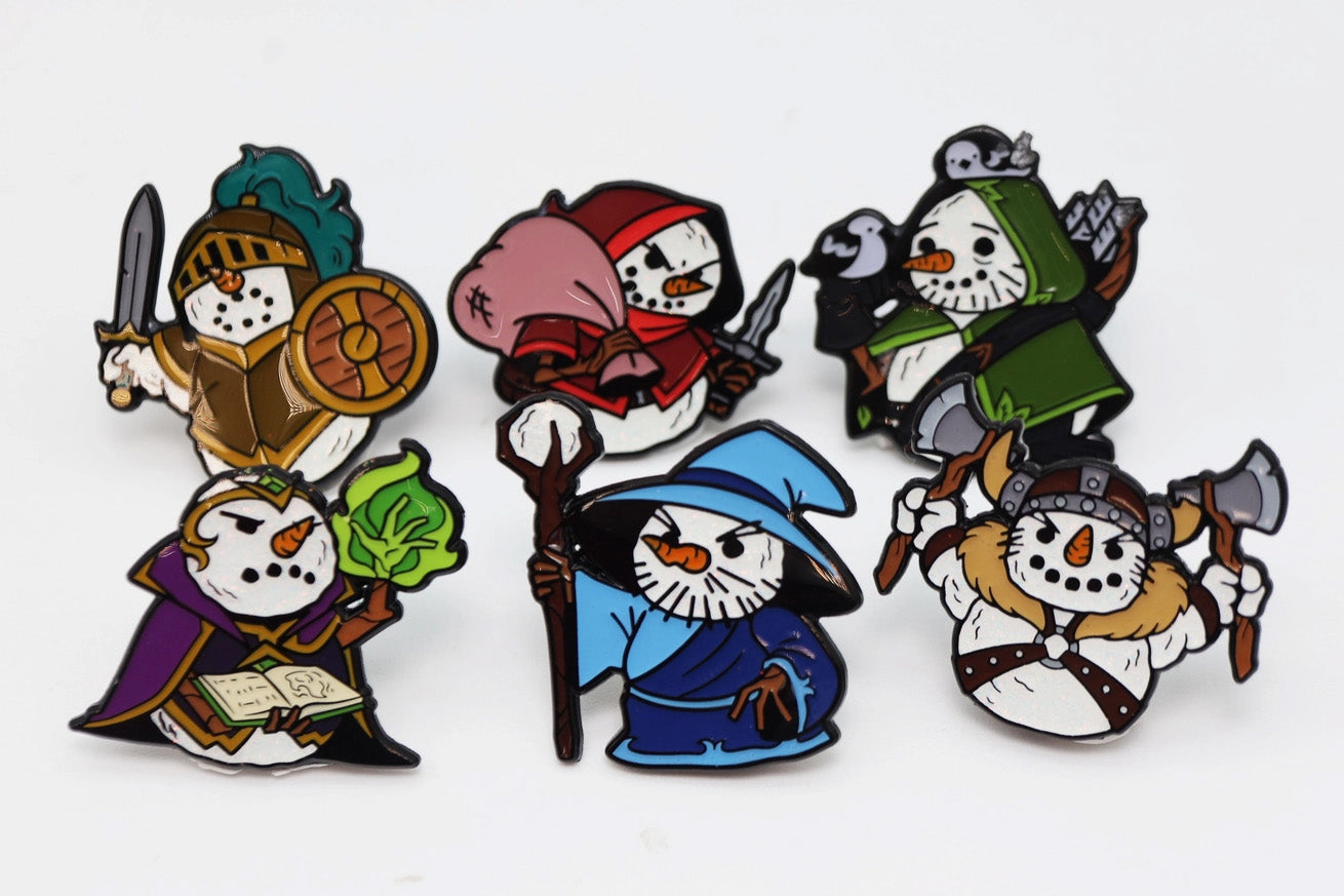 Six colorful Snow Quest enamel pins featuring snowmen dressed as fantasy RPG characters, including a knight, rogue, ranger, wizard, spellcaster, and axe-wielding barbarian, arranged against a white background.