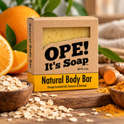 Ope! It’s Soap Natural Body Bar displayed in a warm, modern scene surrounded by fresh oranges, turmeric, oatmeal, and greenery, highlighting its orange essential oil, turmeric, and oatmeal ingredients.