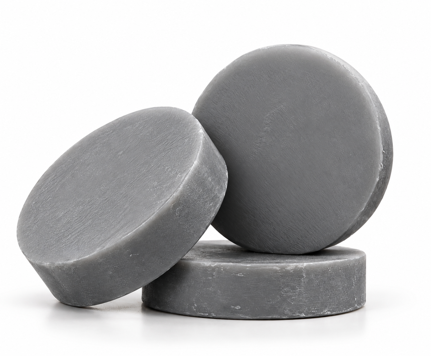 Three round charcoal shampoo bars arranged on a white background, with one lying flat, one tilted at an angle, and one standing upright.