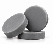 Three round charcoal shampoo bars arranged on a white background, with one lying flat, one tilted at an angle, and one standing upright.