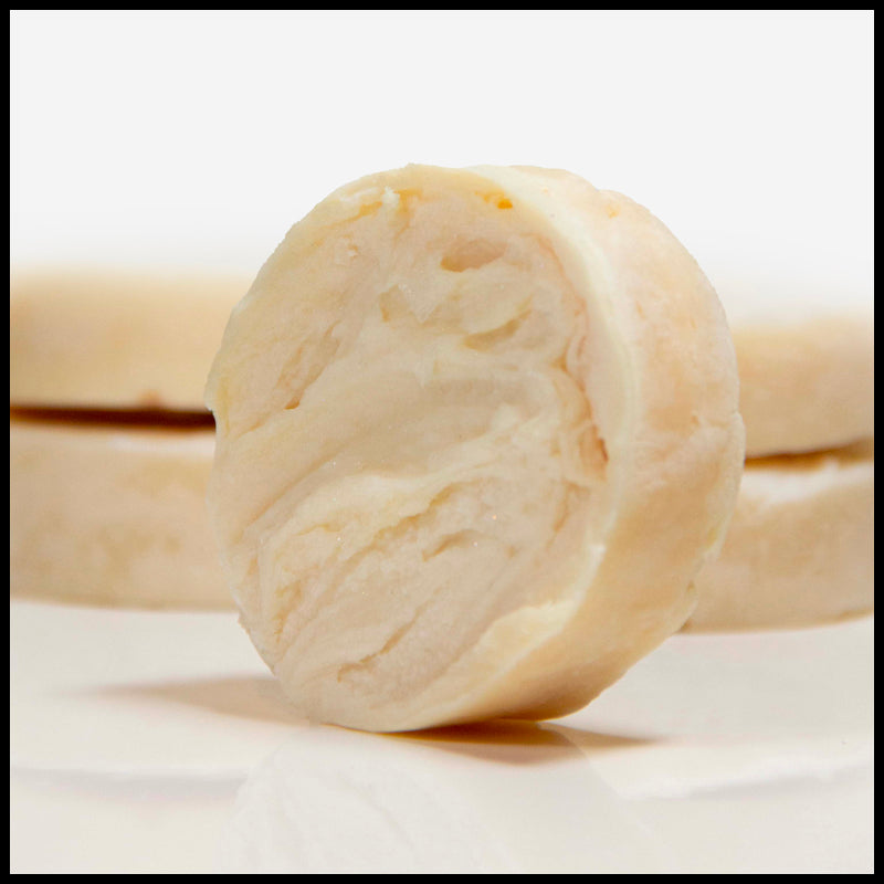 Puck of shave soap standing on its end, with four pucks of shave soap in the background.