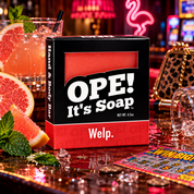 Ope! It’s Soap Welp soap box displayed in a playful bar scene with fresh grapefruit and mint, a spilled pink cocktail, ice, coins, a scratch off ticket, and colorful neon lighting.
