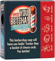 The back view of the Ope! It’s Soap You Betcha! soap box with a dark blue front, red side panel, and barber pole illustration. Visible ingredients on the red panel include Shea Butter, Avocado Oil, Castor Oil, Coconut Oil, and Olive Oil.