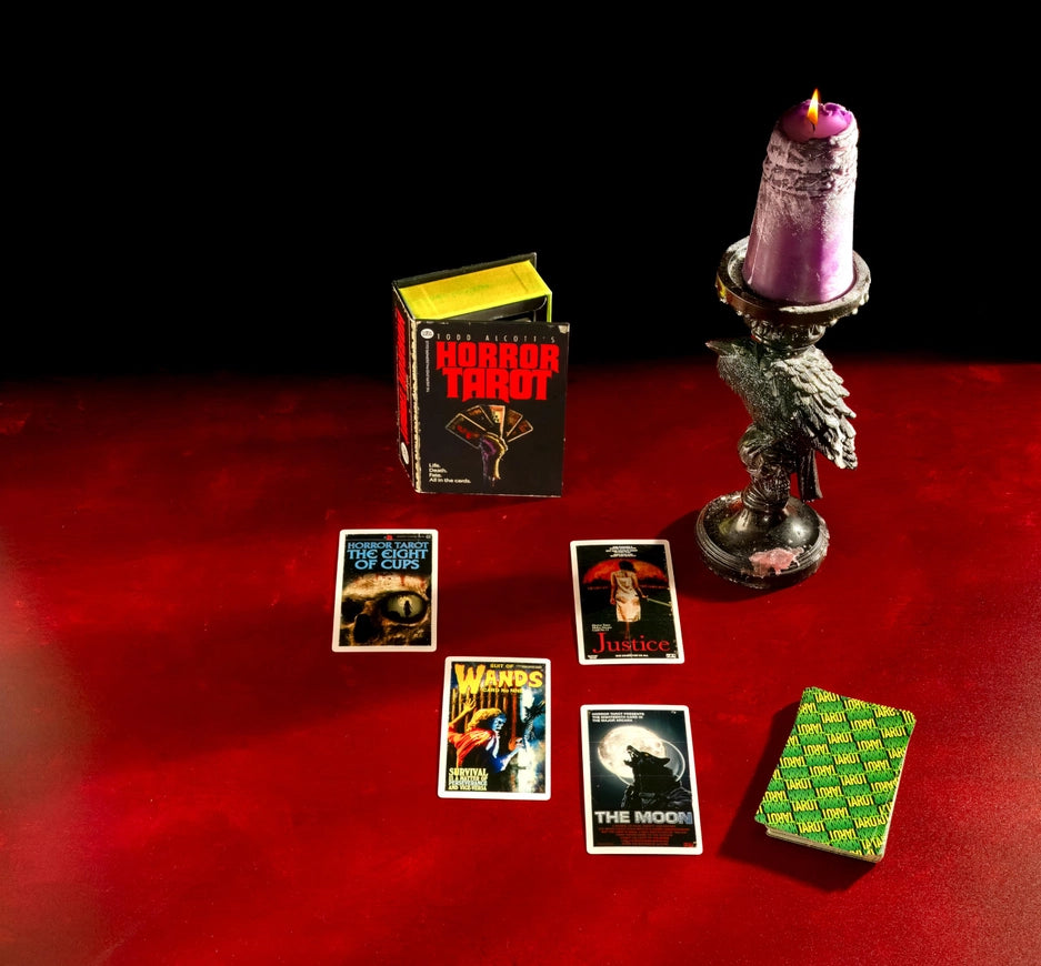 Horror Tarot cards on a red surface with a purple candle and black background