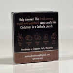 Back side of the Holy Smokes soap. Quote on box says, "Holy smokes! This frankincense, myrrh and patchouli soap smells like Christmas in a Catholic church." Box is black with brown accents.